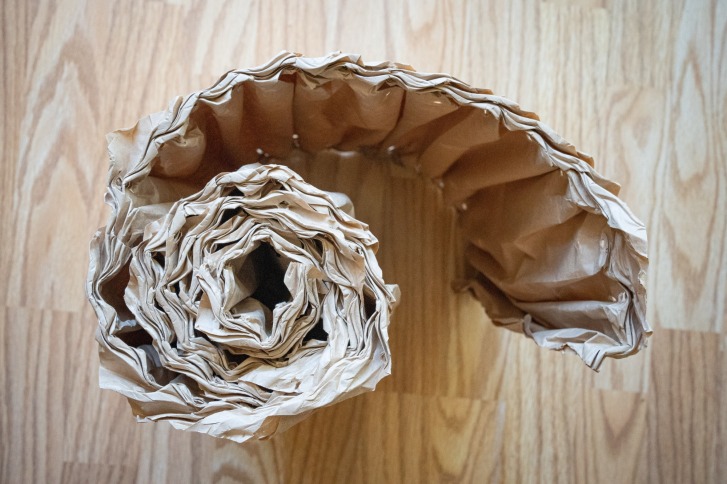 Papieren buis is opgerold in een spiraal op een houten vloer, van bovenaf gezien.