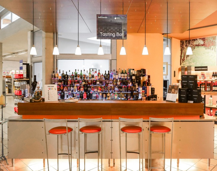 Des tabourets de bar se trouvent devant un bar de dégustation avec de nombreuses bouteilles d'alcool et un panneau au-dessus.