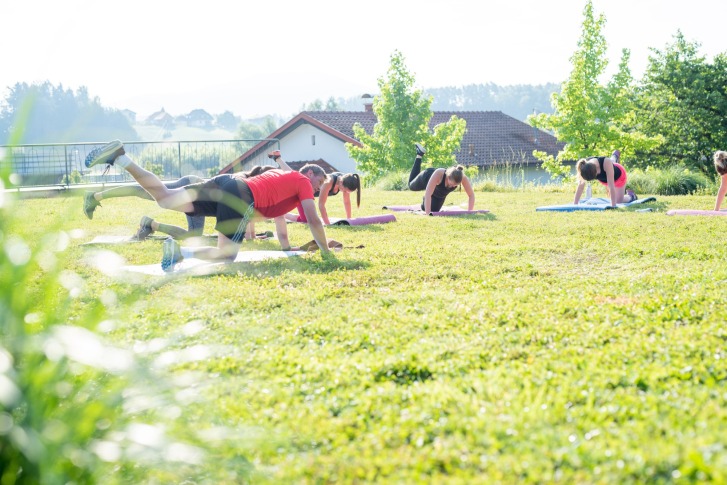 Plusieurs personnes font des exercices de yoga sur des tapis à l'extérieur, sous le soleil.