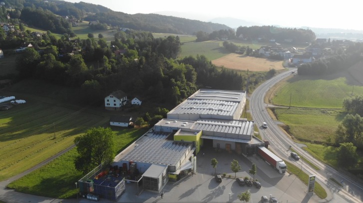 Gebouw met zonnedaken, omgeven door velden en bomen, gelegen aan een weg met auto's.