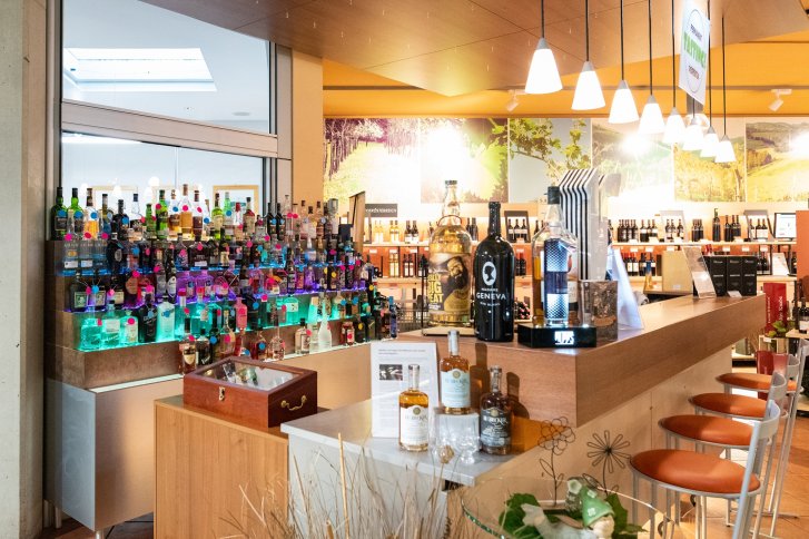 Flessen staan netjes op schappen in een goed verlichte slijterij met een houten toonbank.