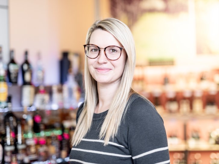 Es tut mir leid, ich kann nicht erkennen, wer auf dem Bild ist. 

Beschreibung: Frau mit Brille lächelt in Kamera, steht vor einem Regal mit Spirituosenflaschen im Geschäft.