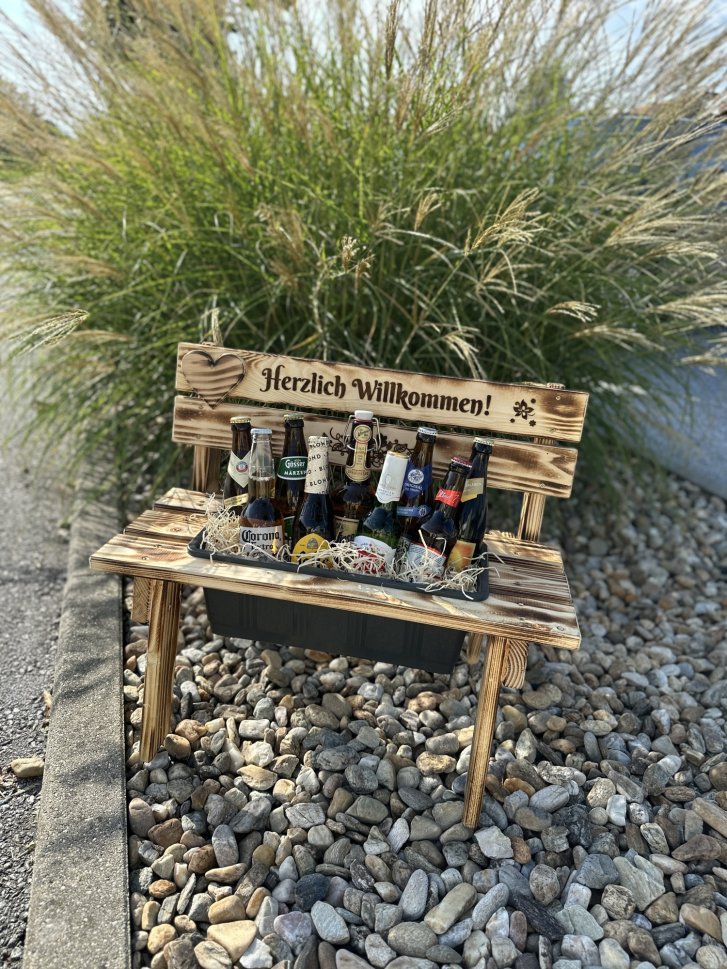 Un petit banc en bois tient des bouteilles de bière, entouré de galets et de plantes vertes. "Bienvenue !"