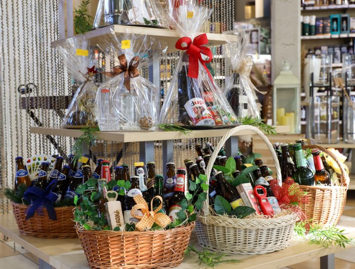 Baskets of beer bottles, decorated with bows, stand on wooden tables in a store.