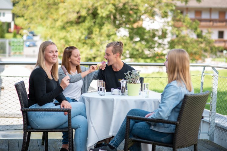 Vier Personen sitzen entspannt draußen am Tisch und genießen Eis in der Sonne.