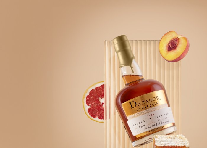 Flasche Rum mit goldenem Etikett schwebt vor Hintergrund mit Pfirsich, Honig und Grapefruit.