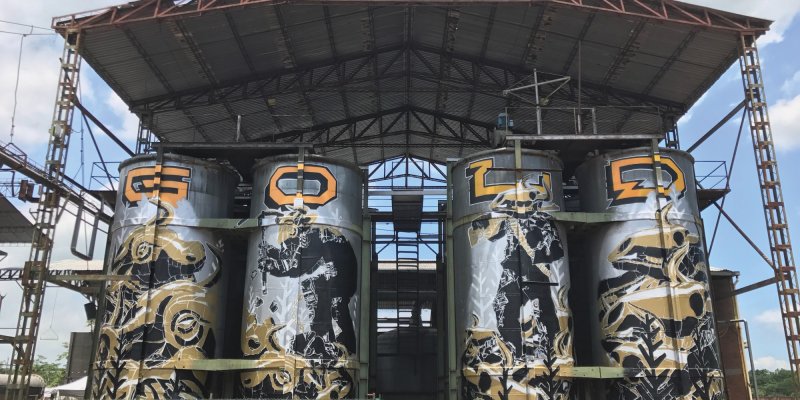 Four painted silos stand under a roof. A man spreads out his arms.