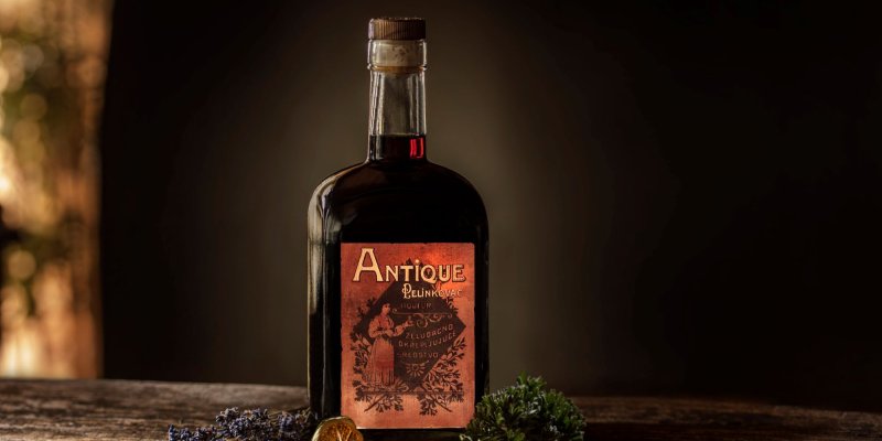 La bouteille avec l'inscription "Antique Pelinkovac" est posée sur un fond en bois, entourée d'herbes et de fruits secs.
