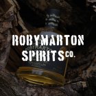 Une bouteille de gin est posée entre des morceaux de bois dans la forêt, avec l'inscription "Roby Marton Spirits Co".
