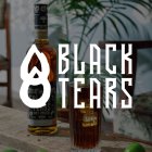 Bottle of rum and glass on wooden table in front of plant, text: "Black Tears".