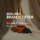 Een jeneverfles staat naast druiven op linnen stof, tekst: "Berliner Brandstifter. Est. 2009".
