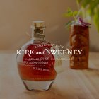 Une bouteille de rhum Kirk and Sweeney Reserva est posée sur une table en bois à côté d'un verre décoratif.