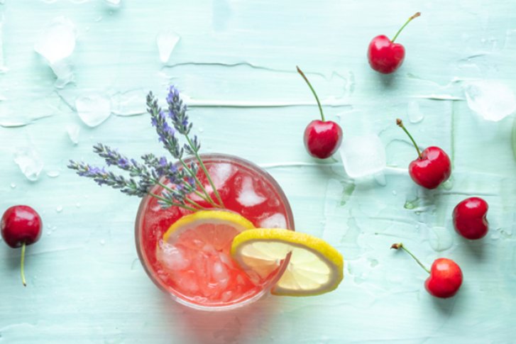 Drei bunte Cocktails mit Obst garniert stehen auf eisbedecktem, hellblauem Tisch mit Kirschen.