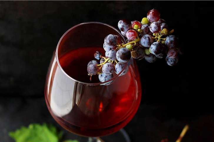 Weinglas mit rotem Wein und Trauben, steht auf dunklem Untergrund.