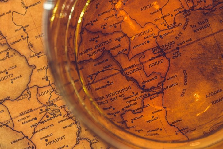 Glas mit Getränk reflektiert auf alter Weltkarte, zeigt Afrika und Arabische Halbinsel.