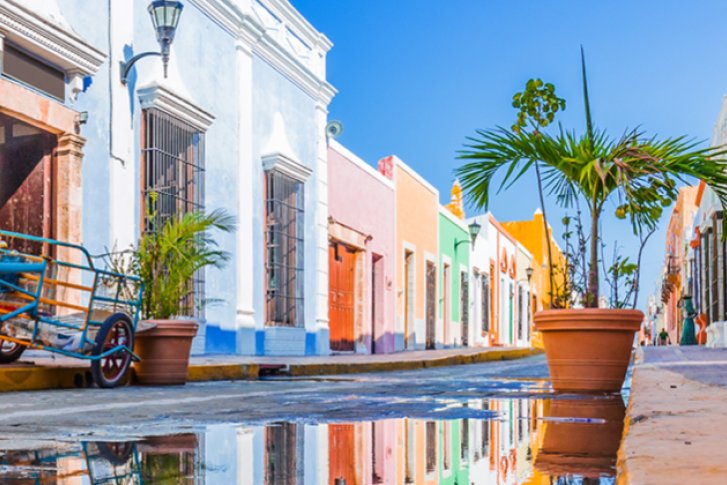 Straße mit bunten Häusern spiegelt sich in Pfütze, dekoriert mit Fahrrad und Topfpflanzen.