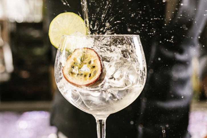 Ein Cocktailglas mit Limette und Eis spritzt in einer Bar-Umgebung mit unscharfem Hintergrund.