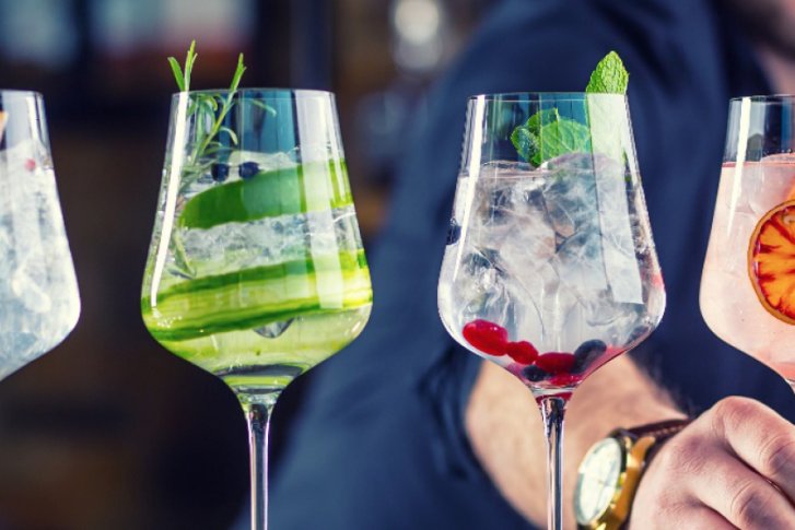 Vier Gläser mit verschiedenen Cocktails, dekoriert mit Früchten, stehen auf einer Bar.