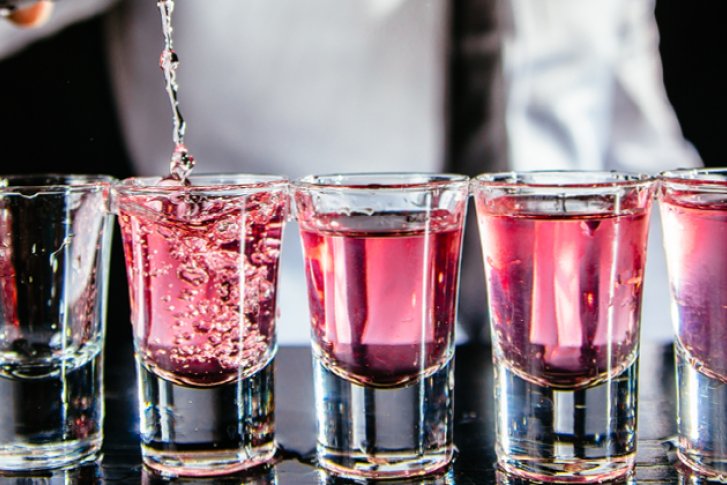 Eine Reihe von Gläsern wird mit rosafarbener Flüssigkeit an einer Bar gefüllt.