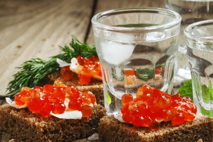 Roggenbrot-Scheiben mit rotem Kaviar, serviert neben Wodkagläsern auf einem rustikalen Holztisch.