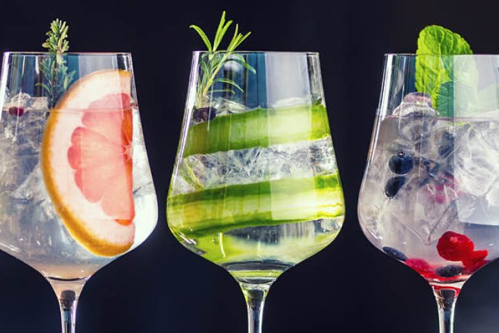 Fünf Weingläser, gefüllt mit Eisscheiben, Zitrusfrüchten und Kräutern, stehen auf einer dunklen Oberfläche.