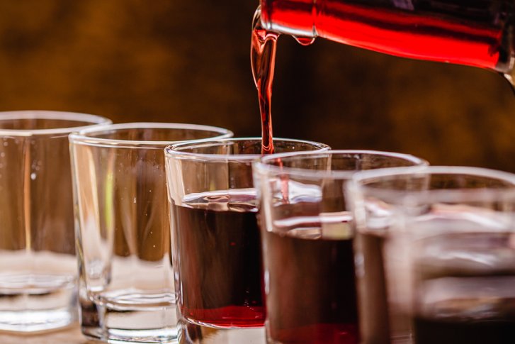 Roter Wein wird in sechs Gläser auf einem Holztisch eingeschenkt.