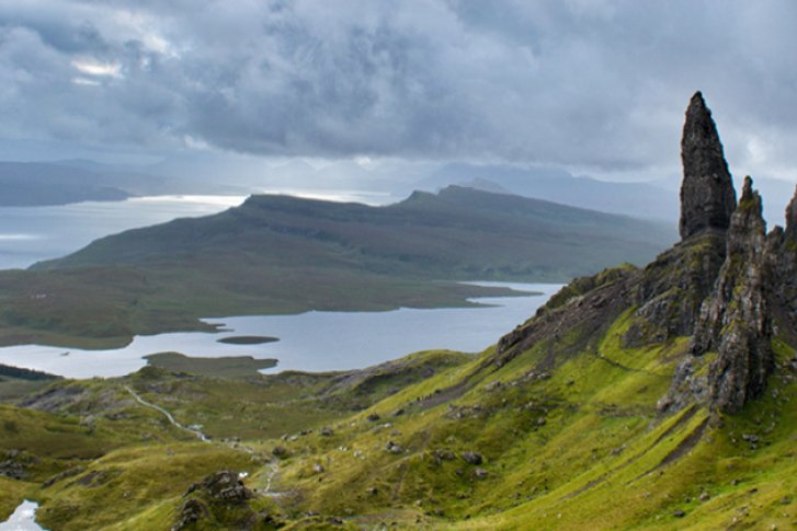 Felsformationen ragen auf grüner Hügellandschaft in die Höhe, während Himmel wolkig darüber liegt.