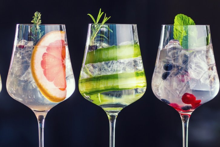 Fünf Weingläser, gefüllt mit bunt dekorierten Cocktails, stehen auf einer dunklen Oberfläche.