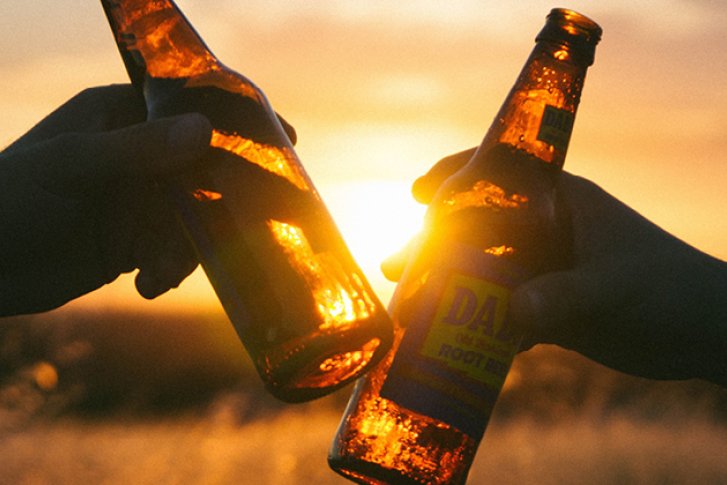 Zwei Bierflaschen stoßen an, leuchten im Sonnenuntergang, im Freien.