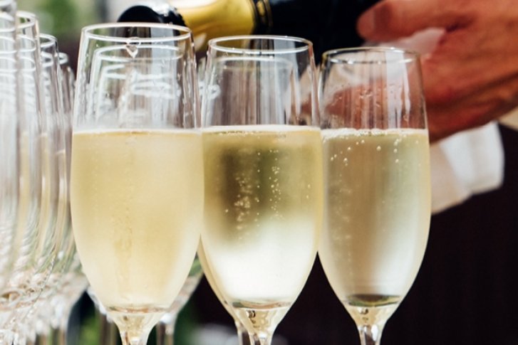 Gläser werden mit Sekt gefüllt; viele leere Gläser im Hintergrund, bei einer Feier.