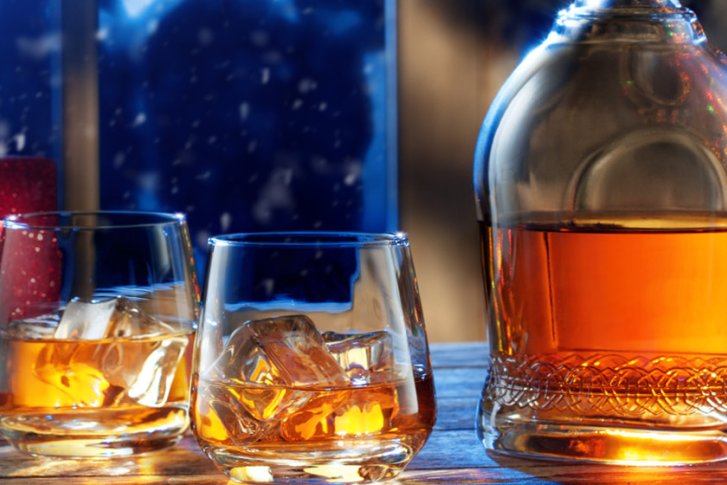 Flasche und Gläser mit goldener Flüssigkeit auf Tisch, umgeben von Geschenken und Weihnachtsbaum.