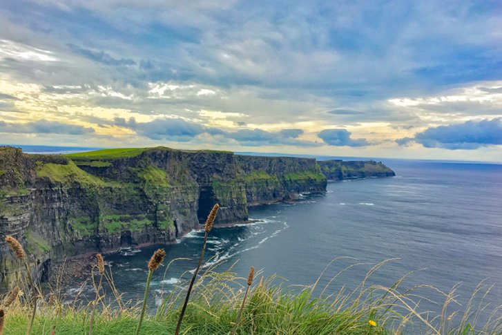 Steile Klippen ragen majestätisch über das ruhige Meer unter bewölktem Himmel empor.