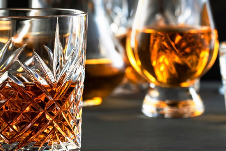 Kristallglas mit Whisky steht auf einem Tisch, umgeben von verschiedenen gefüllten alkoholischen Gläsern.