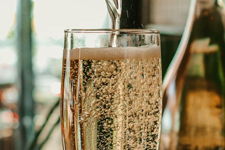 Ein Sektglas wird gefüllt; umgeben von Flaschen und einem weiteren gefüllten Glas in Bar-Atmosphäre.