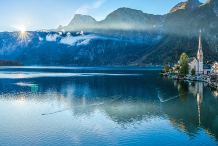 Bergsee spiegelt majestätische Berge, umgeben von malerischen Häusern und herbstlichen Farben.