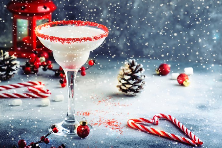 Cocktailglas mit rotem Zucker, steht auf verschneitem Tisch mit Weihnachtsdekoration und Laterne.