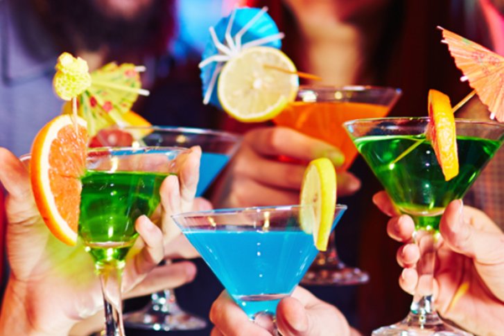 Cocktails werden von Personen in einer festlichen, farbenfrohen Umgebung mit dekorativen Garnierungen gehalten.