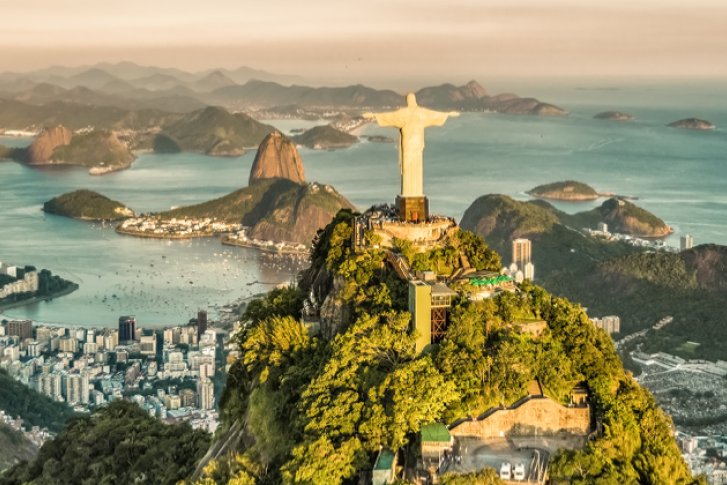 Statue steht auf Berg vor Stadt und Meer, umgeben von grünen Hügeln und Wasser.