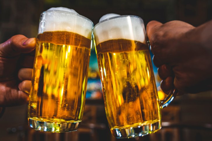 Zwei Bierkrüge stoßen an, in einer gemütlichen, beleuchteten Barumgebung.