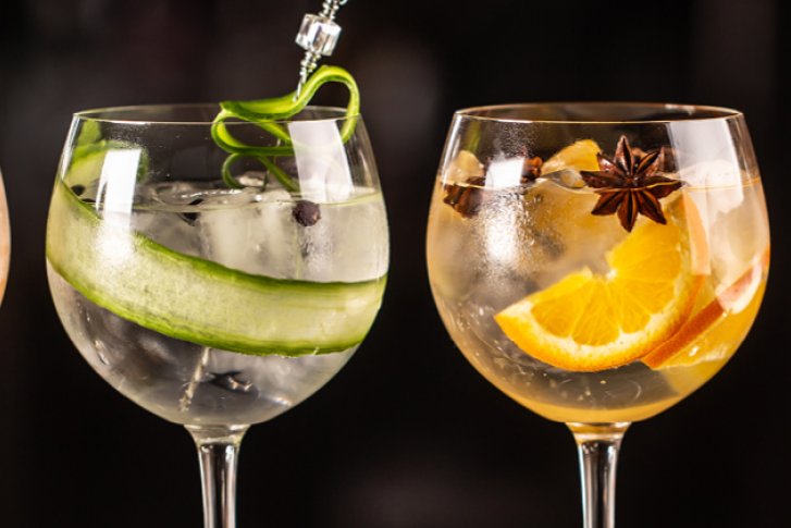 Vier mit Früchten und Kräutern dekorierte Cocktailgläser auf einem dunklen Hintergrund, jeweils unterschiedlich gefüllt.