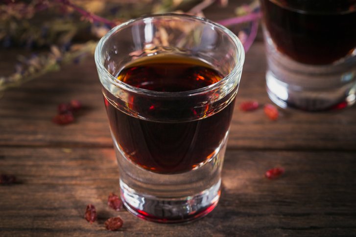 Ein Likörglas mit dunklem Getränk steht auf einem Holztisch, dekoriert mit Trockenfrüchten.