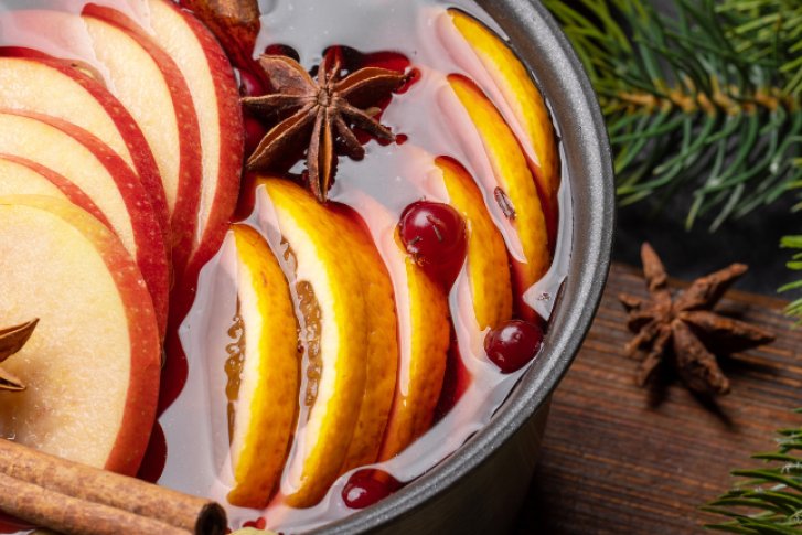 Glühweinglas mit Orangenscheiben und Tannenzweig, umgeben von Gewürzen und Tannenzweigen. (Kopie)