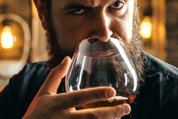 Mann riecht an Glas, konzentriert, in einer gemütlichen, warm beleuchteten Barumgebung.