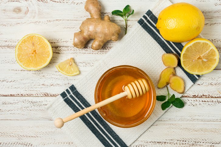 Honig im Glas, umgeben von Zitrone und Ingwer, auf einem Tuch auf Holztisch.