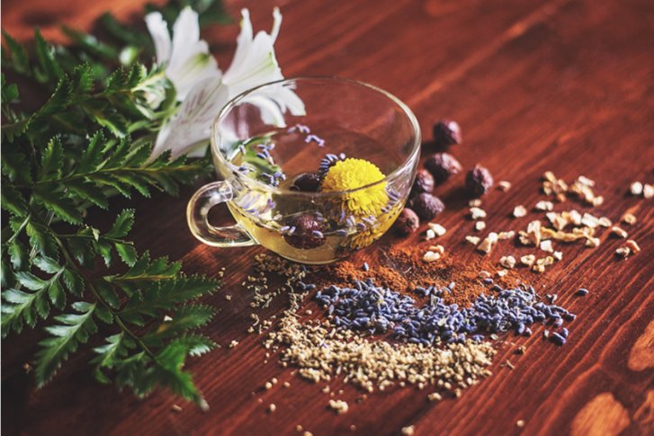 Glas mit Blüte und Gewürzen vor Blumen auf rustikalem Holztisch arrangiert.