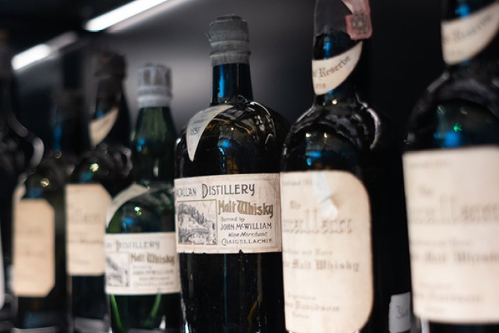 Mehrere Whiskyflaschen stehen dicht nebeneinander in einem beleuchteten Regal.