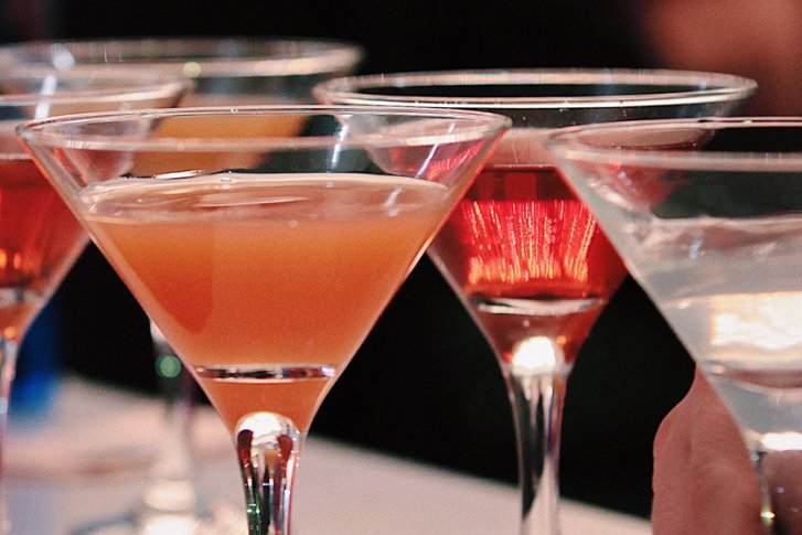 Mehrere Cocktailgläser stehen nebeneinander auf einem Tisch in einer festlichen Umgebung.