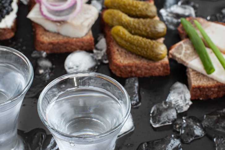 Zwei Gläser Wodka stehen auf eisbedecktem Tisch, begleitet von belegten Canapés.