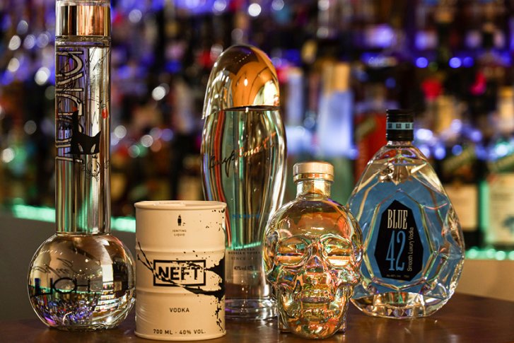 Verschiedene Flaschen stehen nebeneinander auf einem Tisch, Hintergrund ist eine beleuchtete Bar.