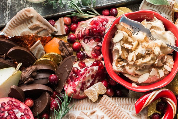Schüssel mit Dessert, umgeben von Schokolade, Keksen, Granatapfel, auf einem rustikalen Holztisch arrangiert.
